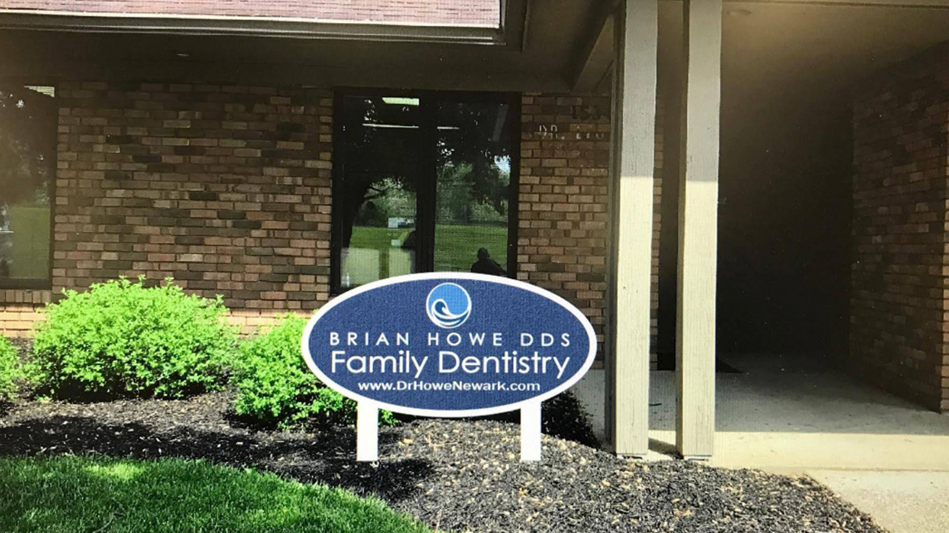 The image shows a sign for  Brian Powell Family Dentistry  outside a building with a brick facade, under a clear sky.