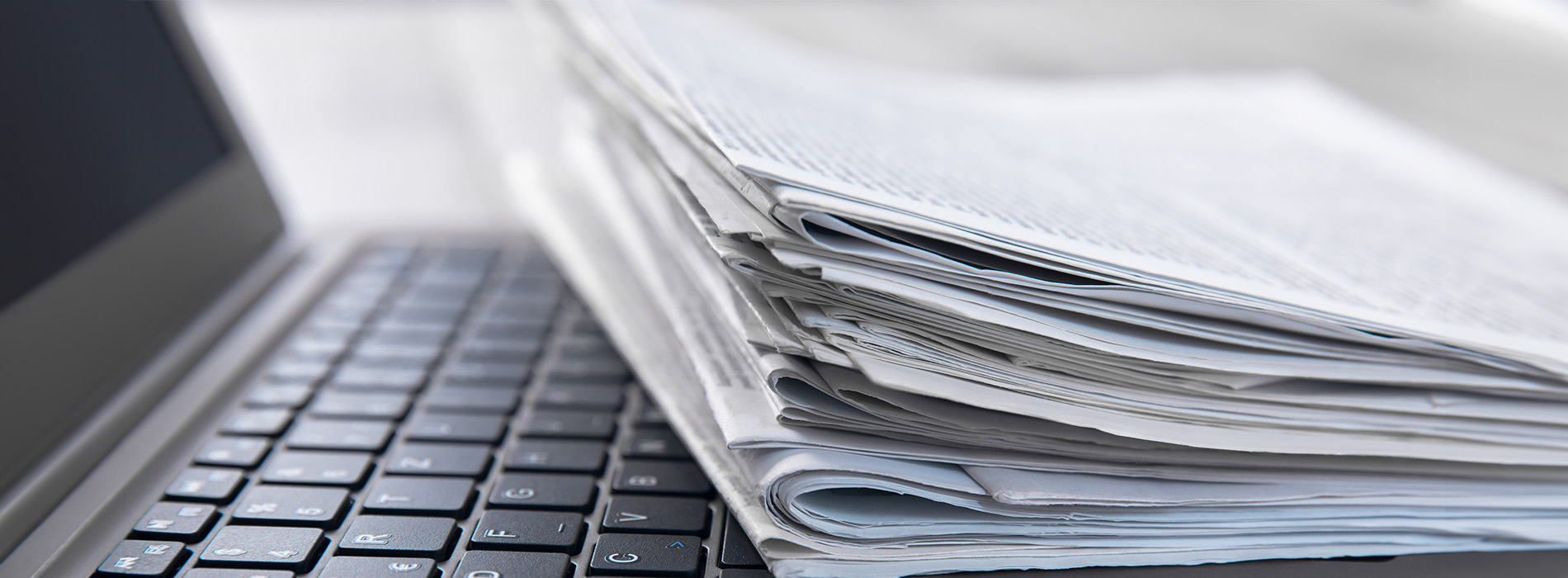 The image displays a stack of papers lying on top of a laptop computer, with the focus on the papers rather than the laptop itself.