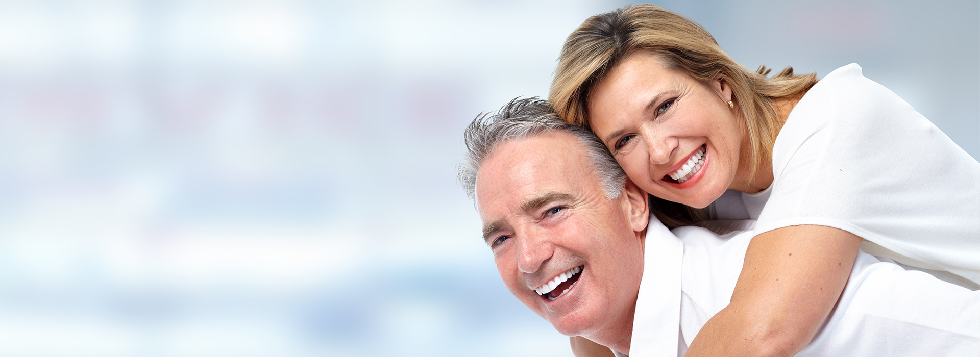 A photograph of a smiling older couple embracing and posing together with warm lighting and a blurred background.