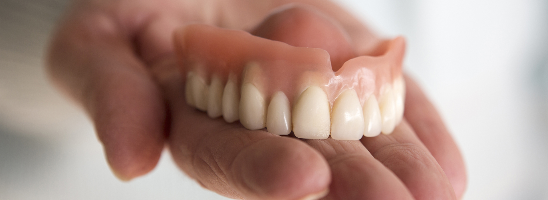 An elderly hand holding a set of dentures with visible teeth stains.