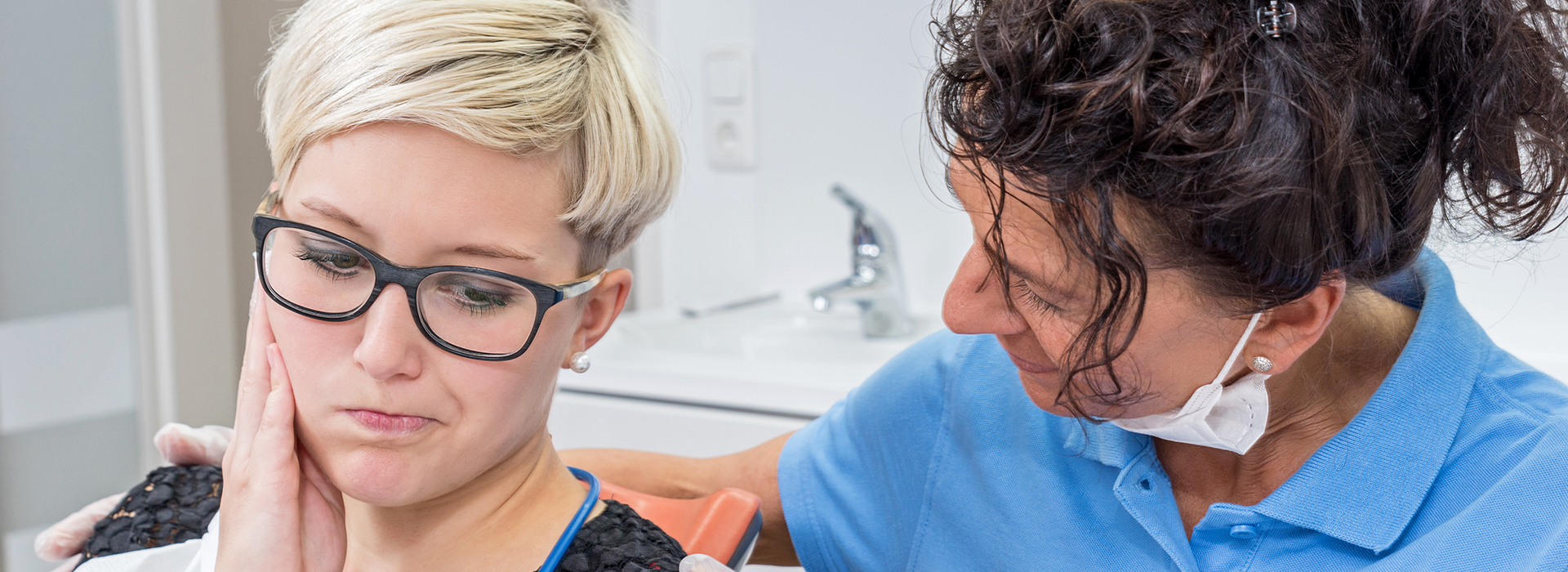 The image depicts a dental care setting with a woman receiving dental treatment from a dentist, who is wearing glasses and has short hair.
