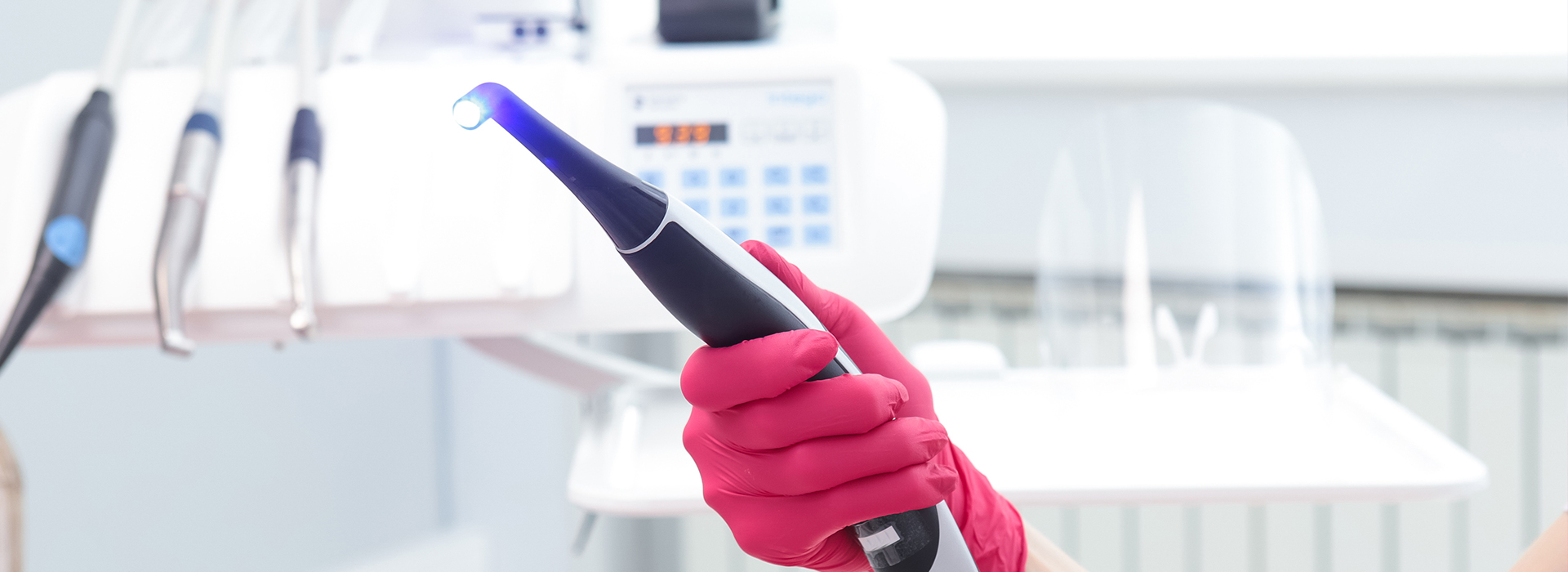 The image shows a person holding a blue device with a red glove on their hand, standing in front of a counter with various items, including what appears to be a medical device and a bottle.