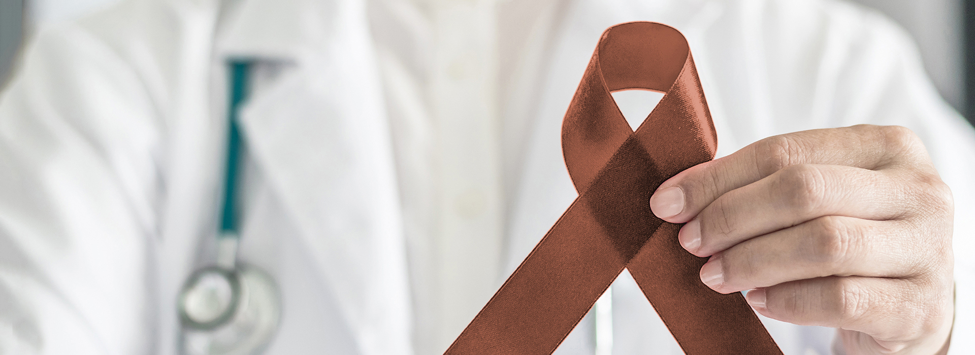 The image features a medical professional holding a red ribbon with an  A  symbol in their hand, set against a blurred background that suggests a hospital environment.