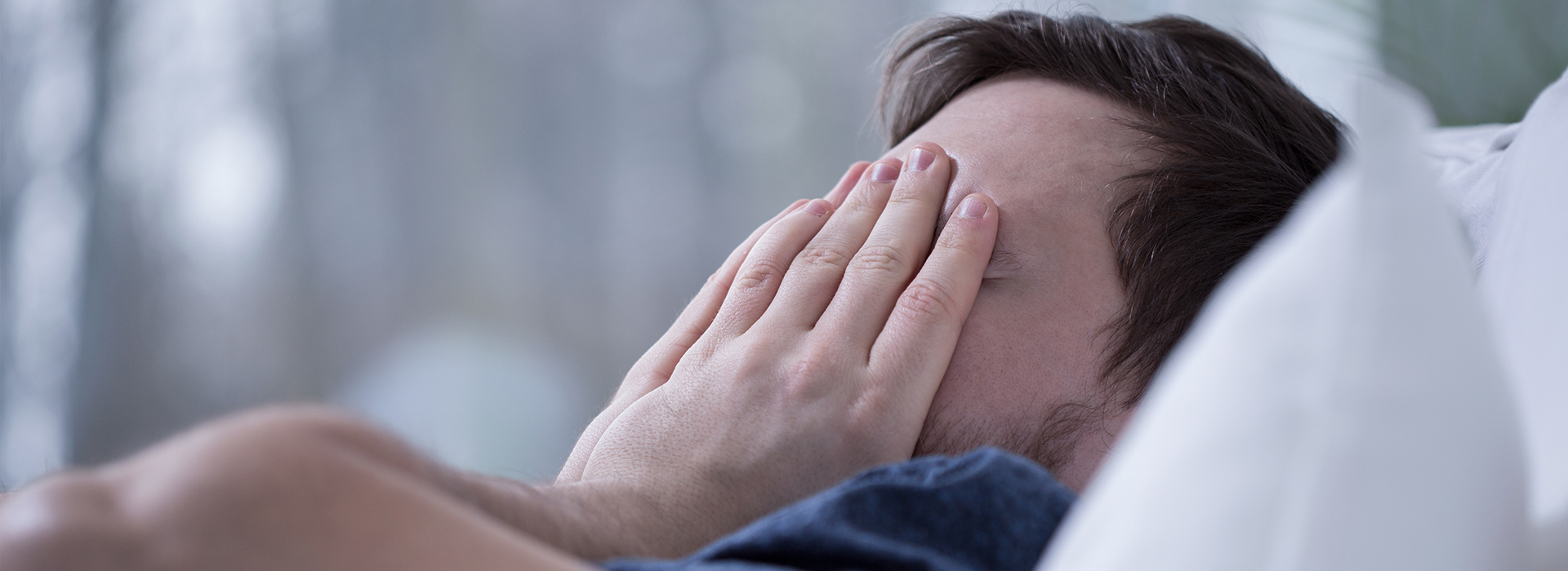 The image depicts a person lying down with their face covered by their hands, appearing to be in a state of distress or sadness.