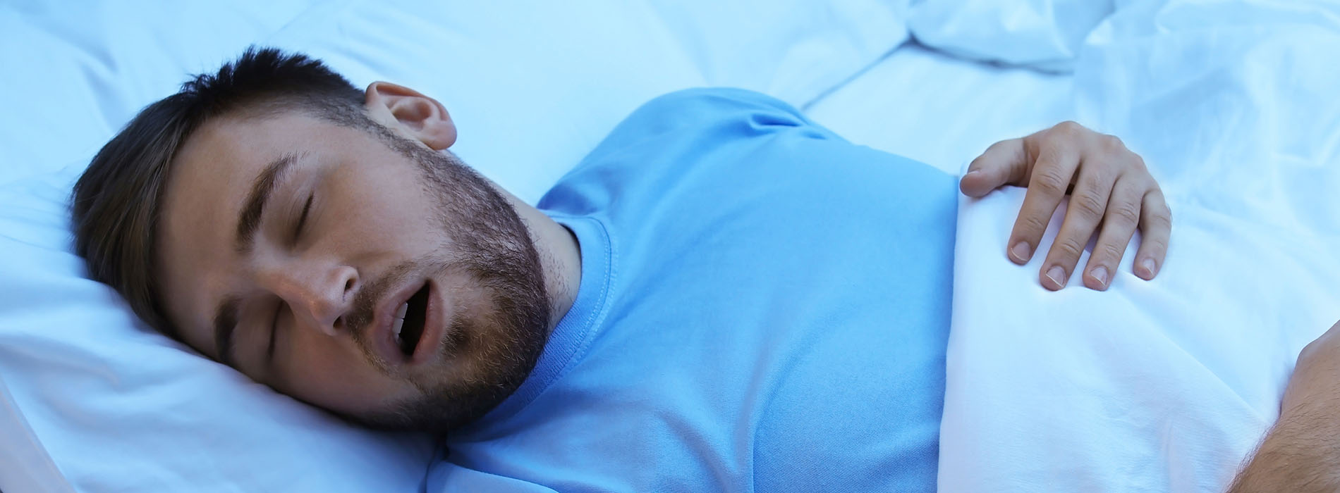 The image shows a man lying down with his eyes closed, appearing to be asleep, with a white pillow under his head on a bed with blue sheets.