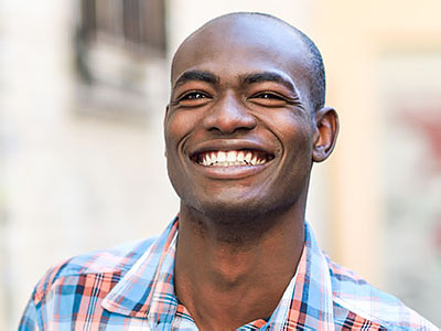 A smiling man with short hair, wearing a blue shirt, stands against a backdrop of an urban street scene.
