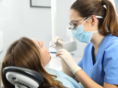 A dental hygienist performing oral care procedures on a patient s teeth while seated in a dental chair.