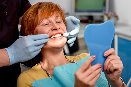 A woman sitting in a dental chair with a blue mouth guard, smiling broadly at the camera, while a dental professional attends to her teeth.
