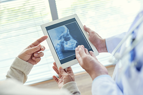 A medical professional, possibly a radiologist or surgeon, is using an iPad to display an X-ray, with the patient s hand holding a tablet showing the same X-ray, both in a hospital setting.