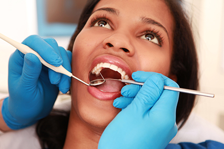 A woman receiving dental treatment with a professional holding tools over her mouth.