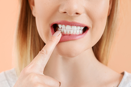 A woman with her finger on her teeth, showing a smile with a toothbrush in her mouth.