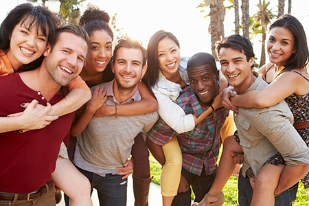 A group of people, predominantly young adults, are posing together for a photograph with smiles on their faces, embracing each other in a celebratory manner, during daylight outdoors.