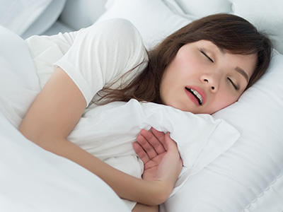 A woman sleeping peacefully on a bed with her eyes closed, wearing a white t-shirt.